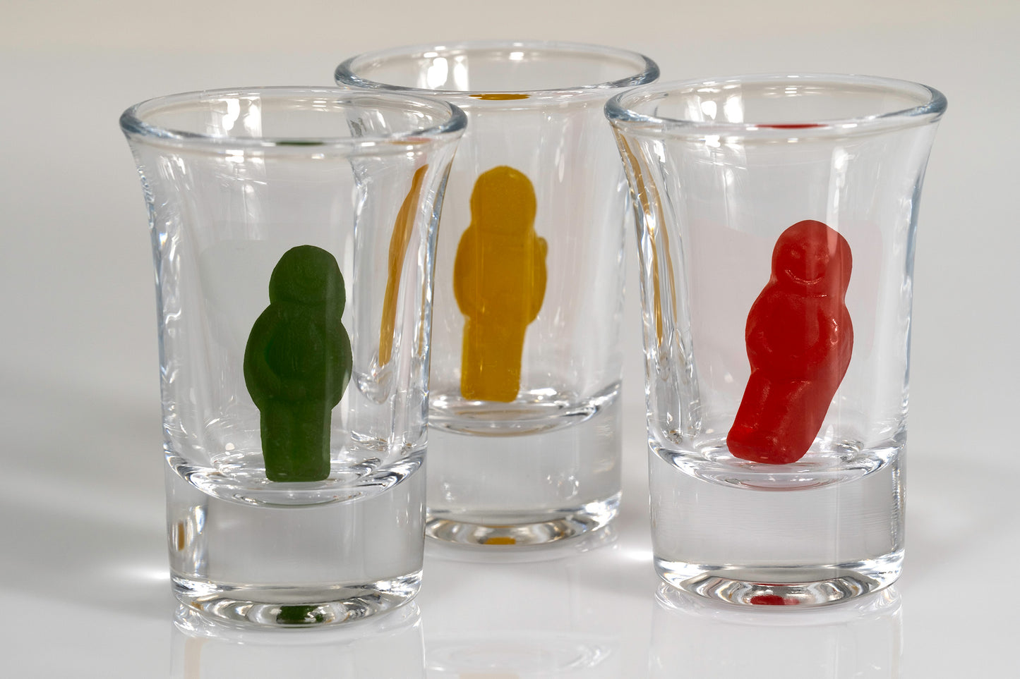 Contemporary still life of three clear shot glasses containing green, yellow and red miniature figures.