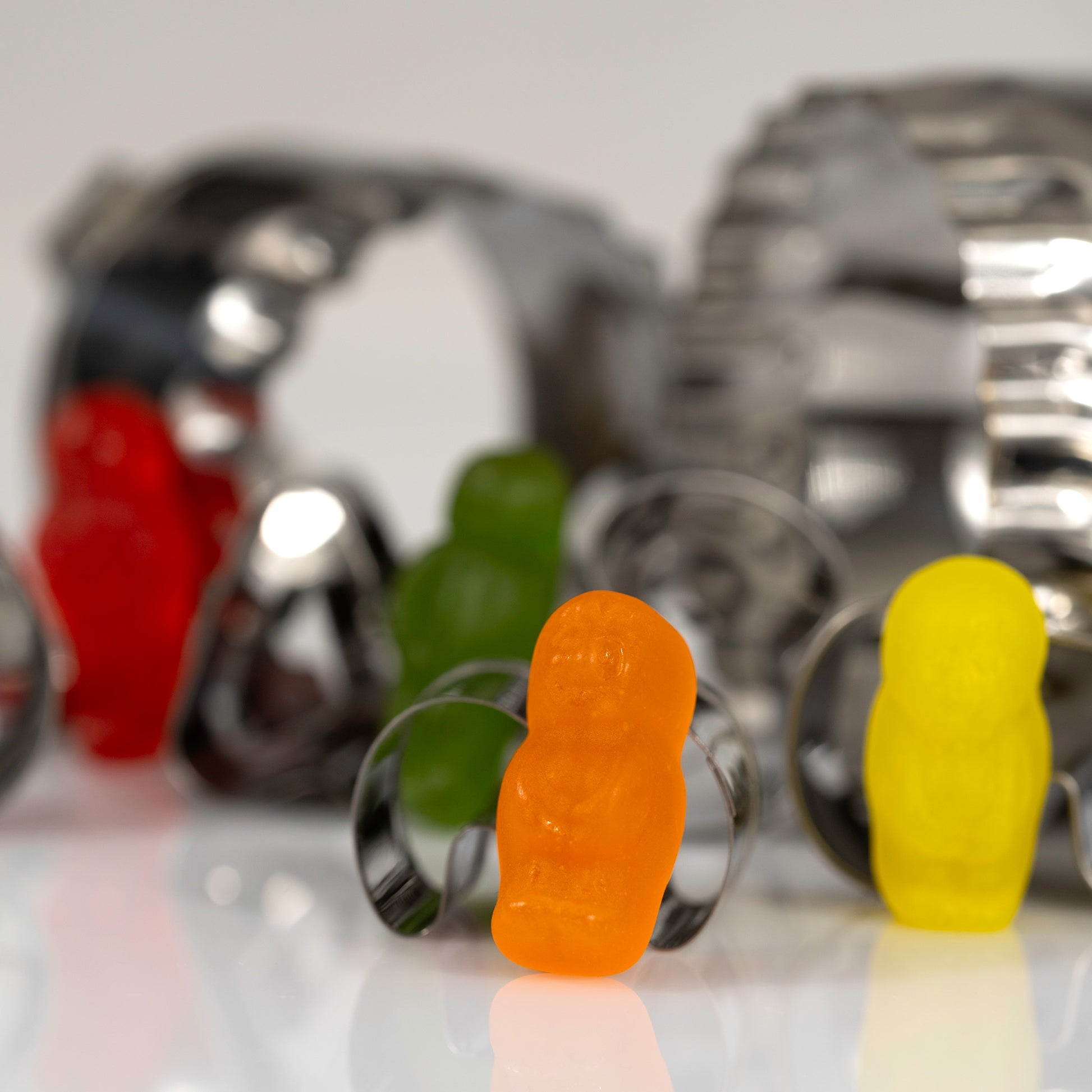 Orange miniature figure in sharp focus surrounded by colourful figures and blurred reflective metal baking cutters.