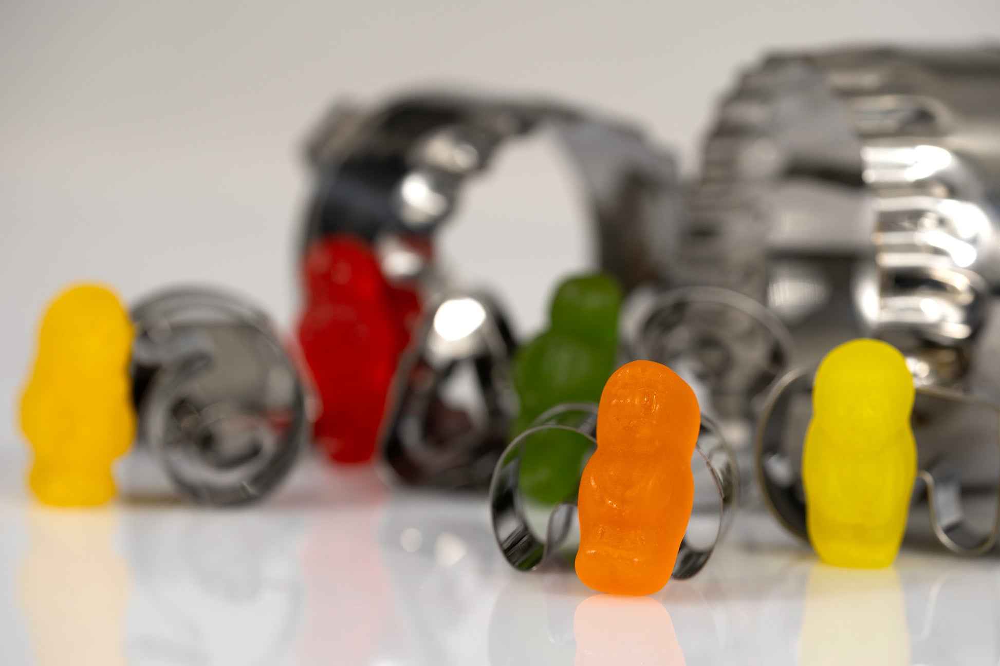 Orange, yellow, green and red miniature figures standing independently among scattered metal baking cutters.