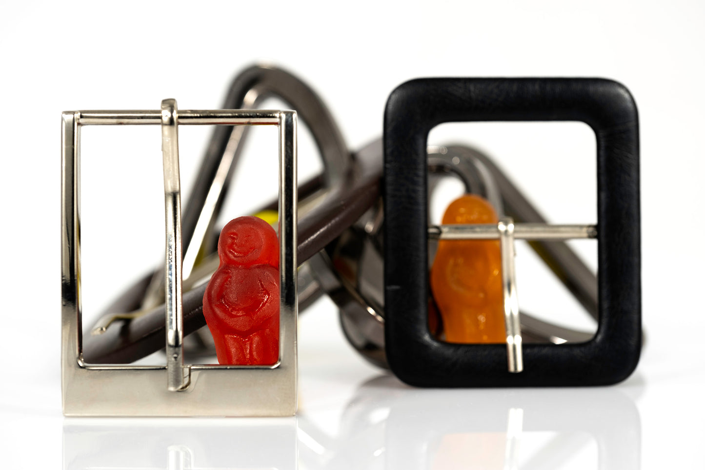 Miniature red and orange figures surrounded and framed by overlapping metal and black belt buckles.