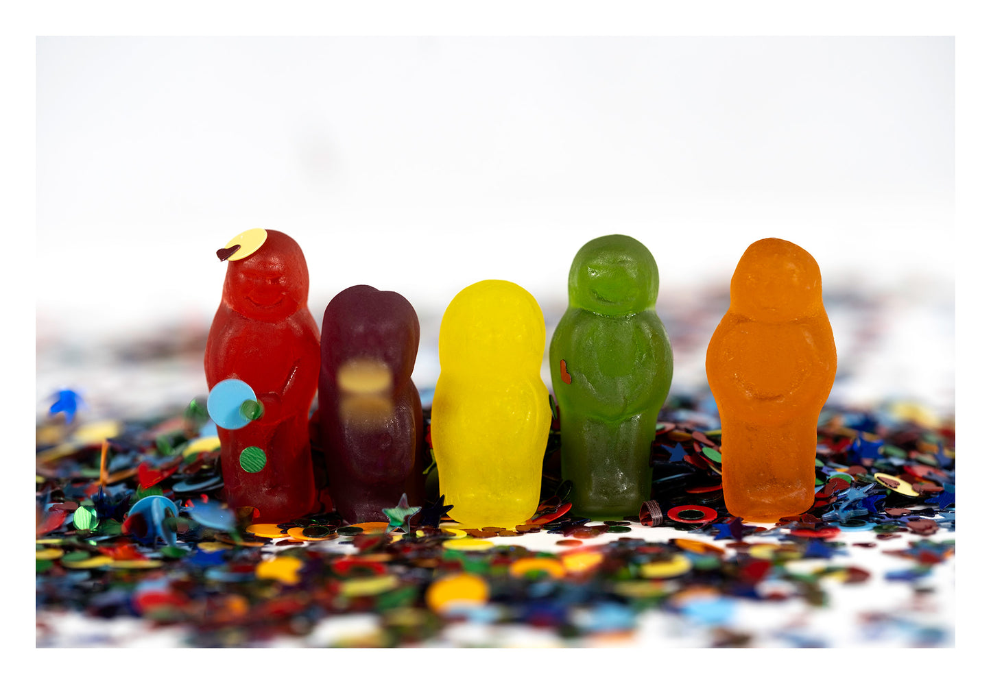 Five colourful miniature figures standing in scattered multicoloured confetti against a bright white background.