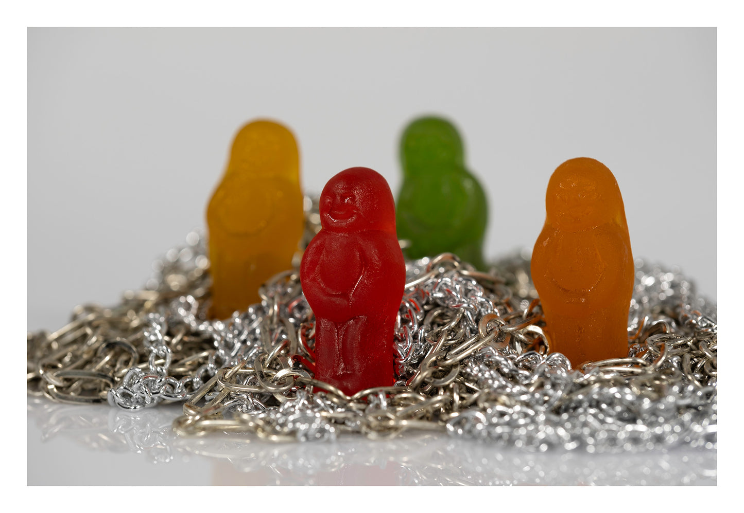 Four colourful miniature figures standing among tangled silver and metallic chains against a pale background.