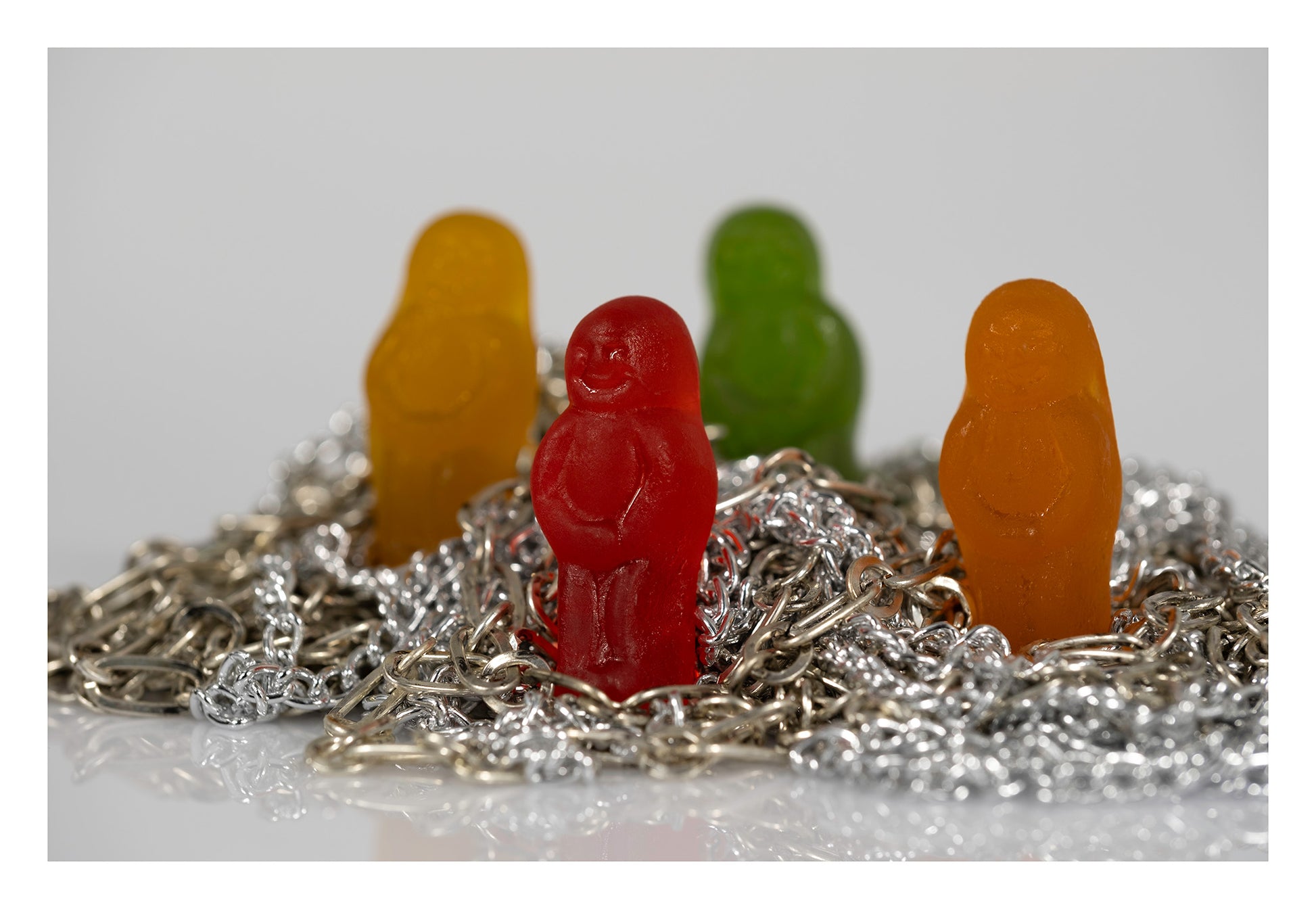 Four colourful miniature figures standing among tangled silver and metallic chains against a pale background.