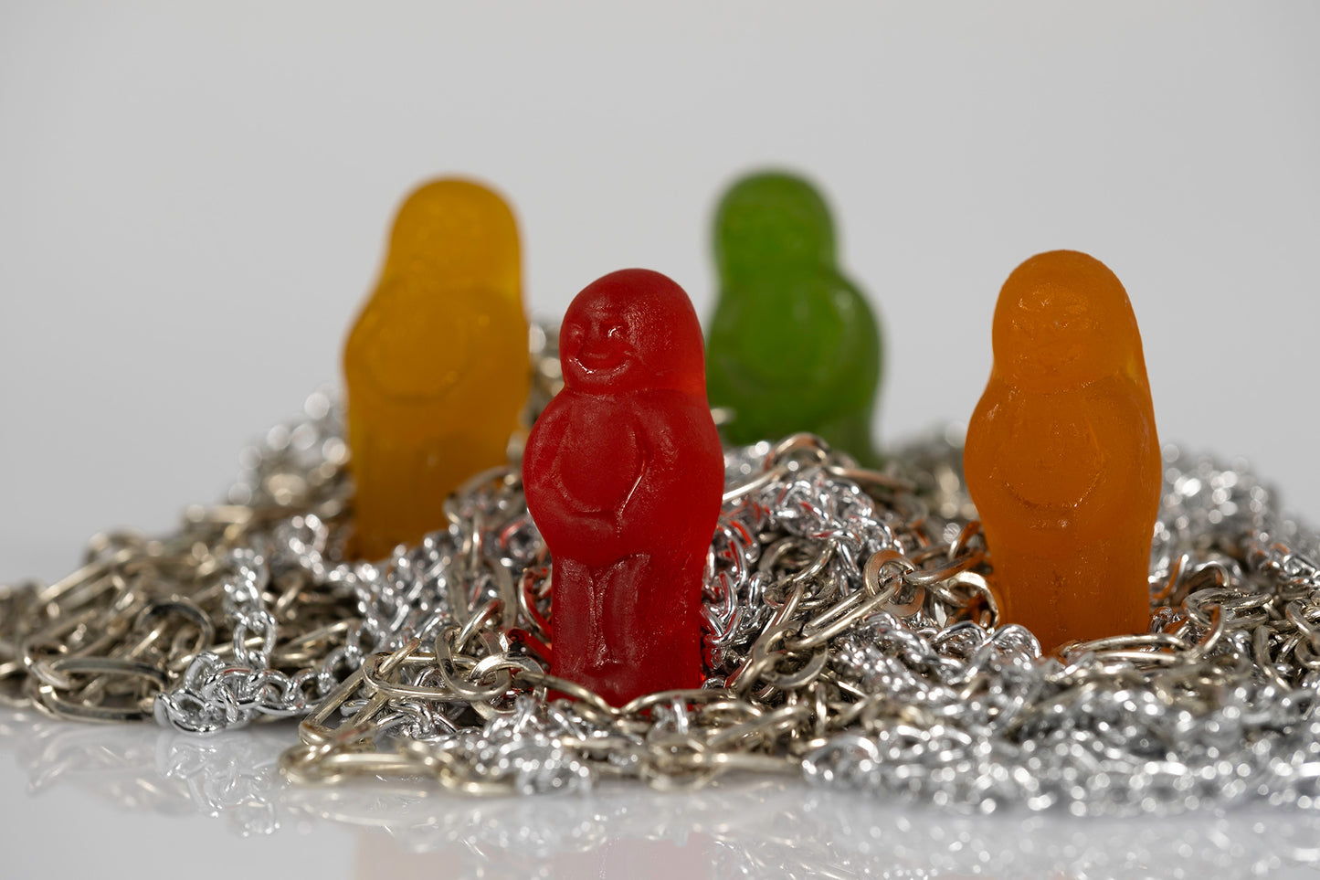 Red, yellow, green and orange miniature figures emerging from a dense arrangement of tangled metallic chains.