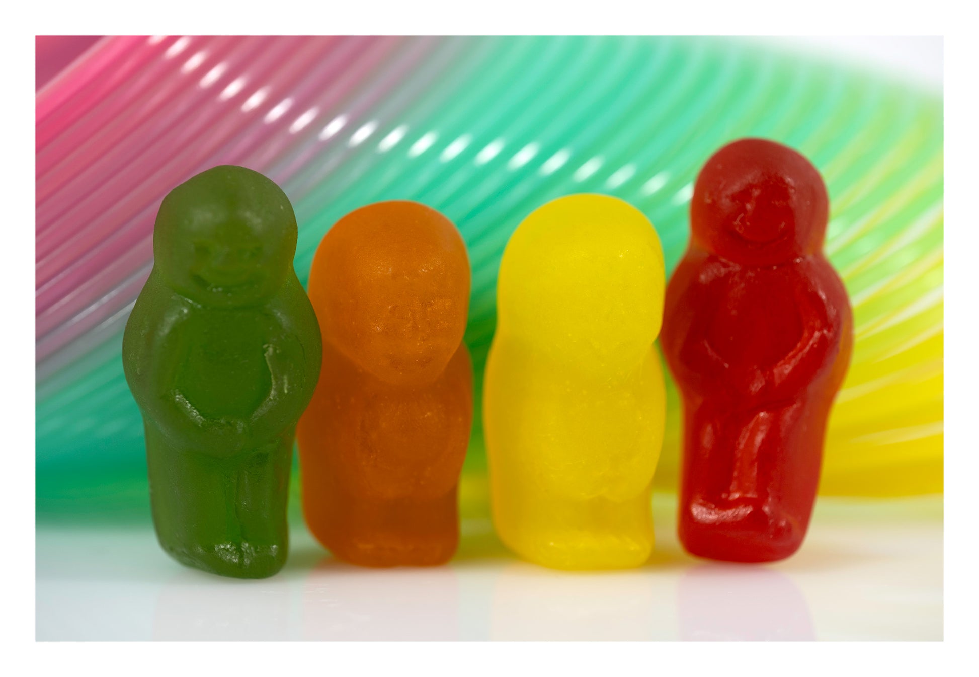 Four green, orange, yellow and red miniature figures standing against sweeping bands of pink, turquoise, green and yellow.
