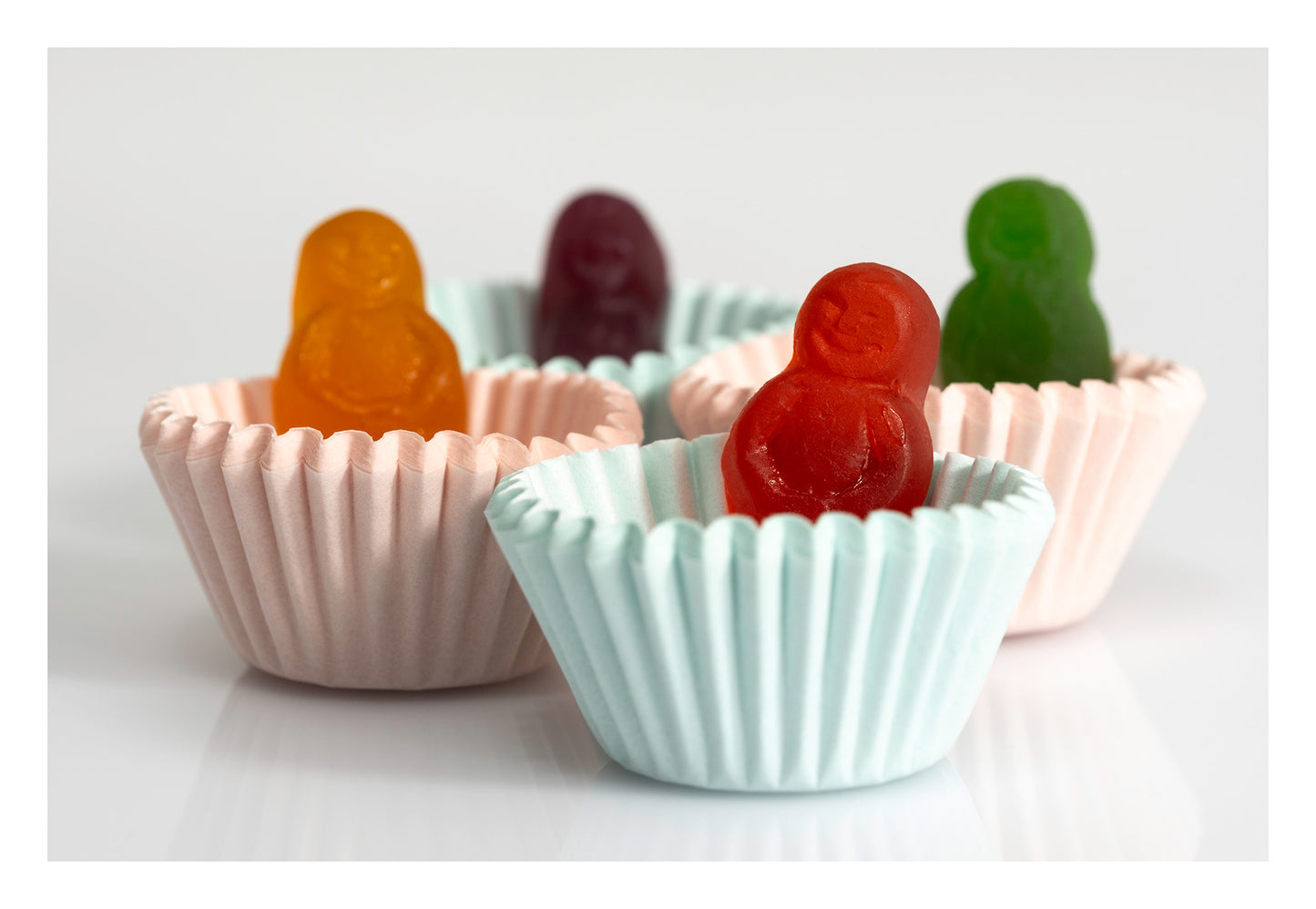 Colourful miniature figures sitting inside pale pink and blue cupcake cases against a white background.