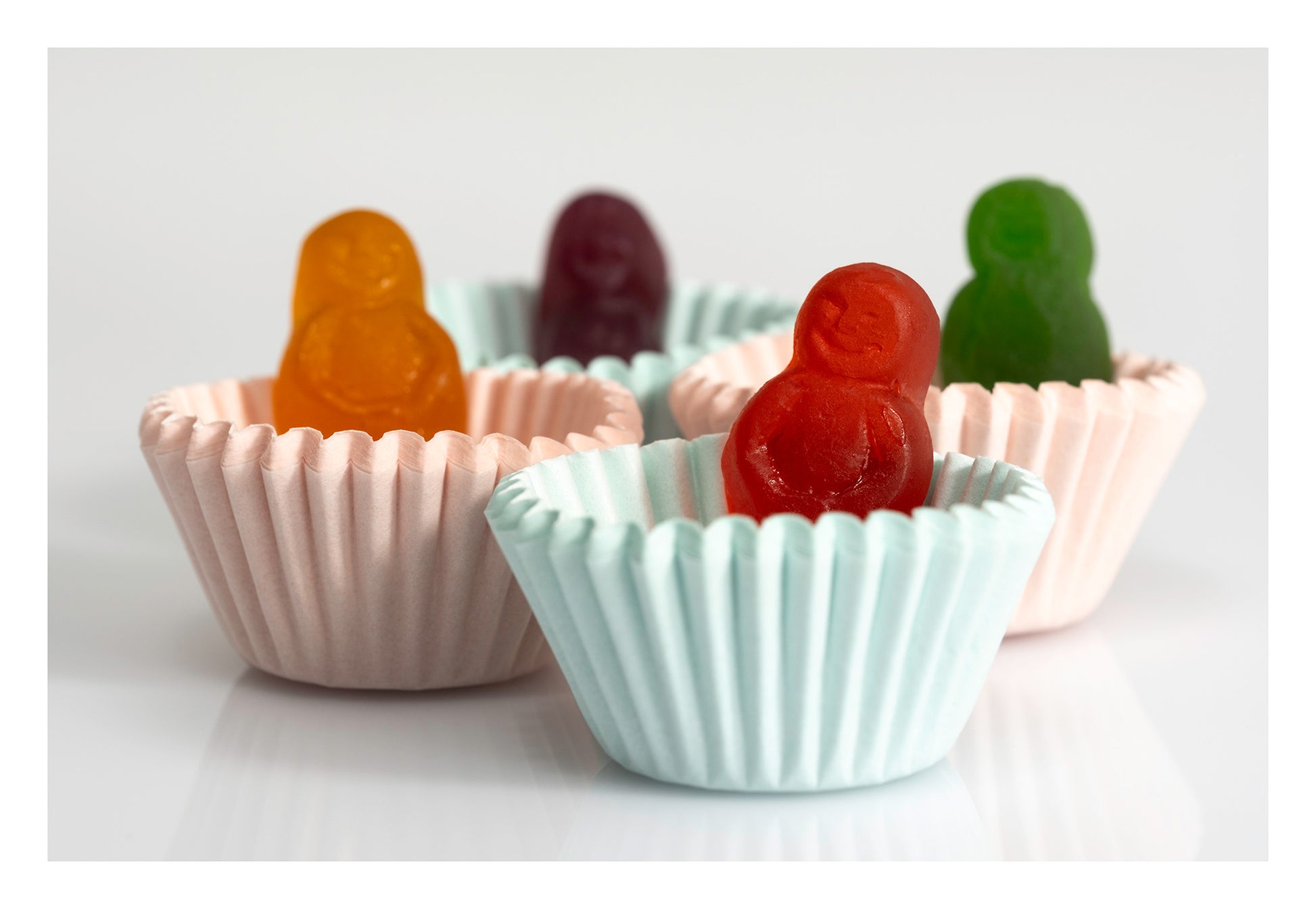 Colourful miniature figures sitting inside pale pink and blue cupcake cases against a white background.