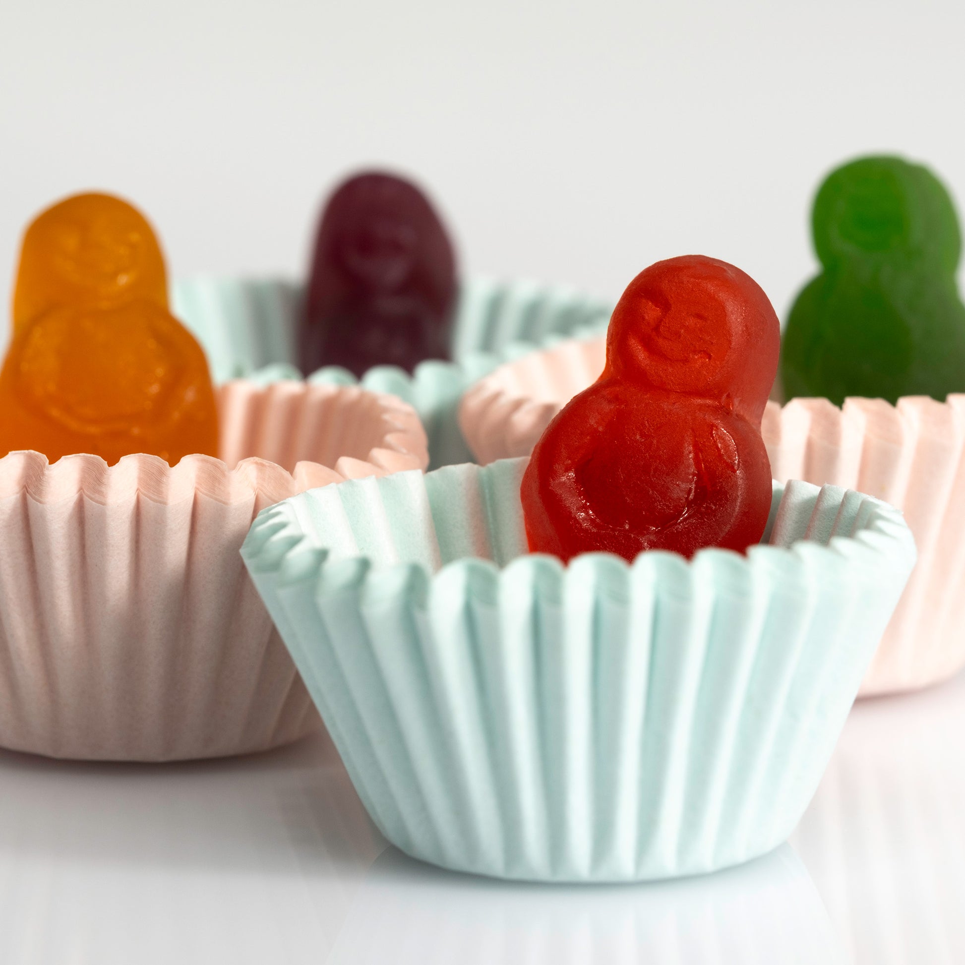 Close-up of a red miniature figure sitting in a pale blue cupcake case with orange, purple and green figures behind.