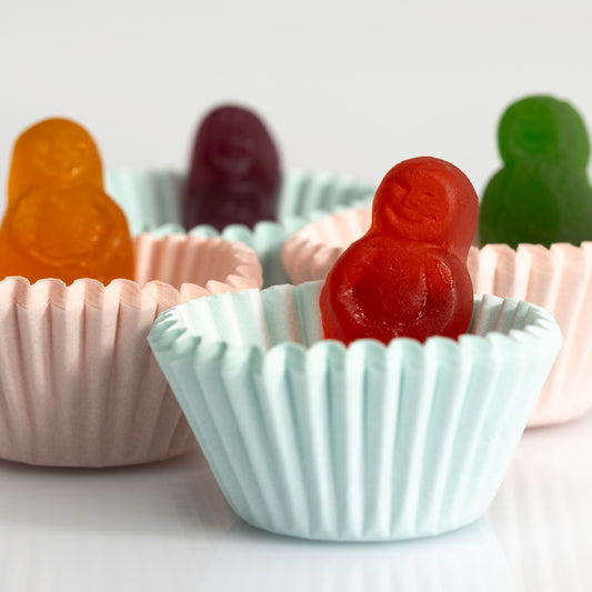 Close-up of a red miniature figure sitting in a pale blue cupcake case with orange, purple and green figures behind.