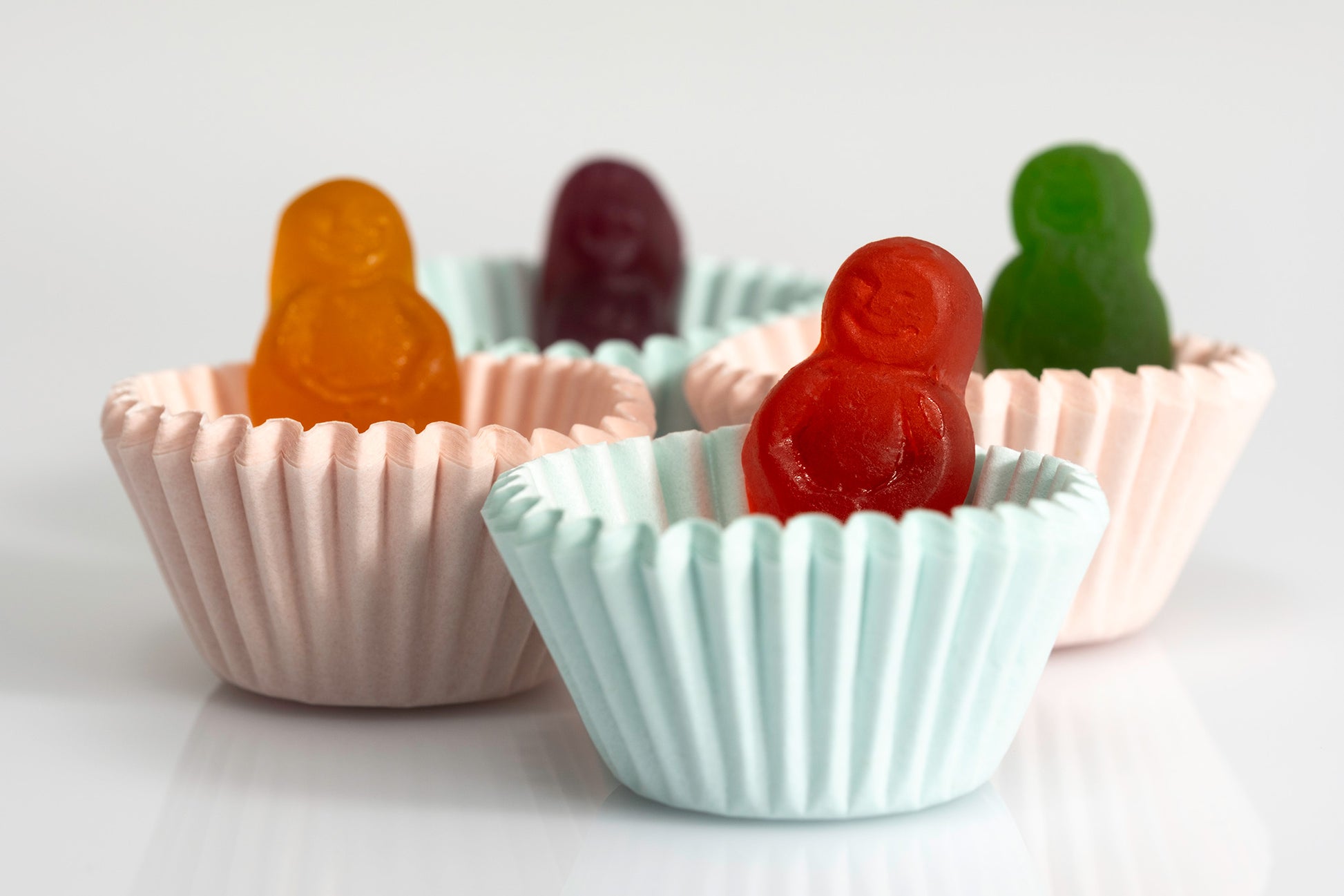 Red, orange, purple and green miniature figures arranged individually inside pastel cupcake cases.