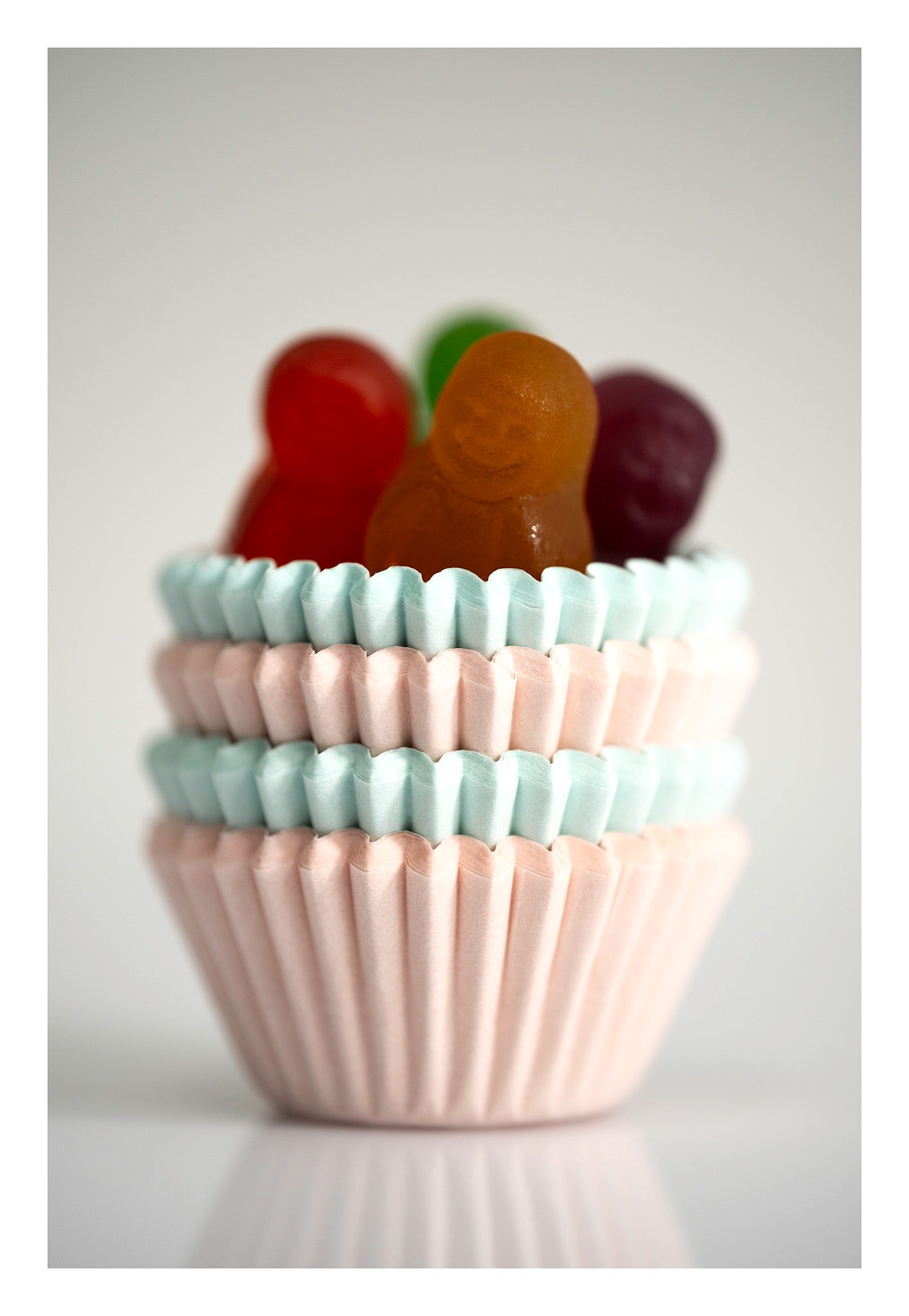 Colourful miniature figures emerging from stacked pale pink and blue cupcake cases against a soft white background.