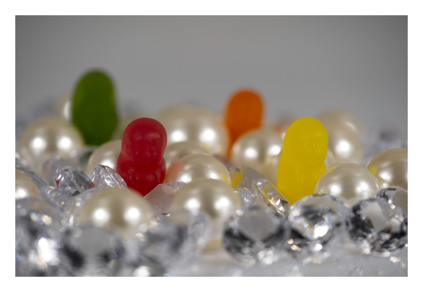 Red and yellow miniature figures among oversized imitation pearls and clear faceted objects, with green and orange figures softly focused behind.