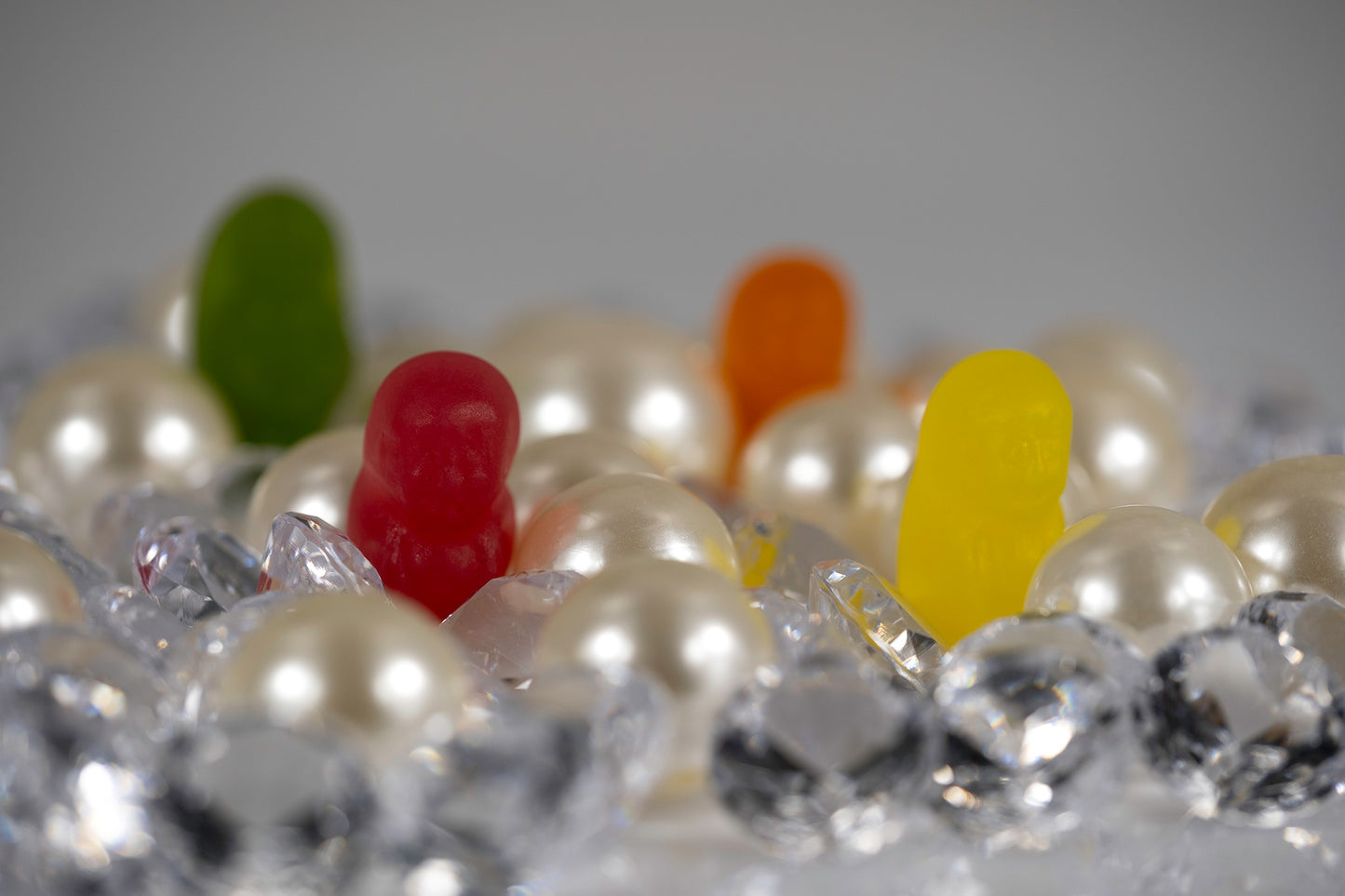 Four colourful miniature figures appearing within a landscape of oversized pearls and clear faceted decorative objects.