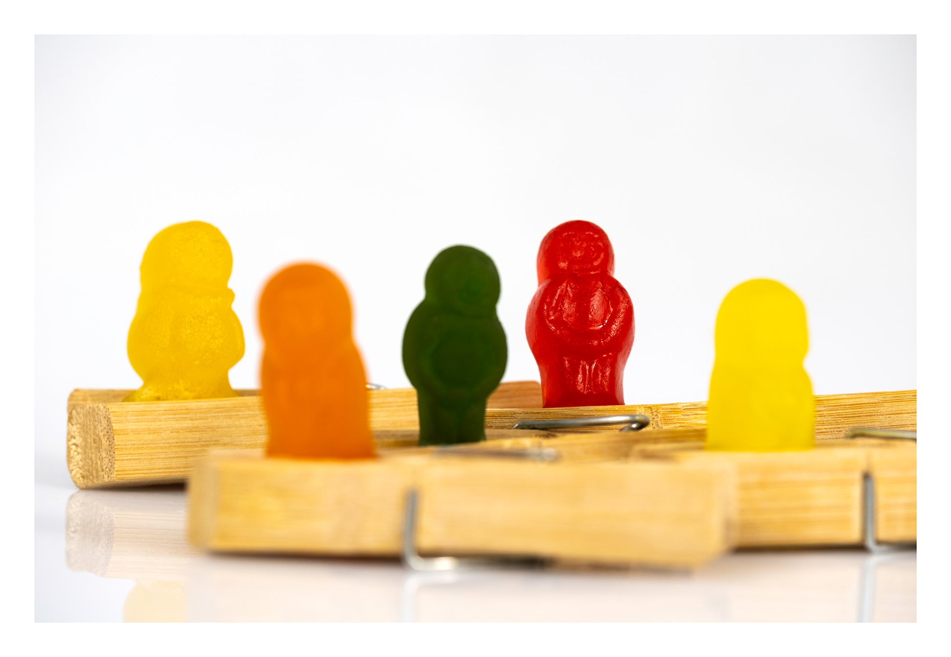 Colourful gummy figures positioned among overlapping wooden clothes pegs against a bright white background.