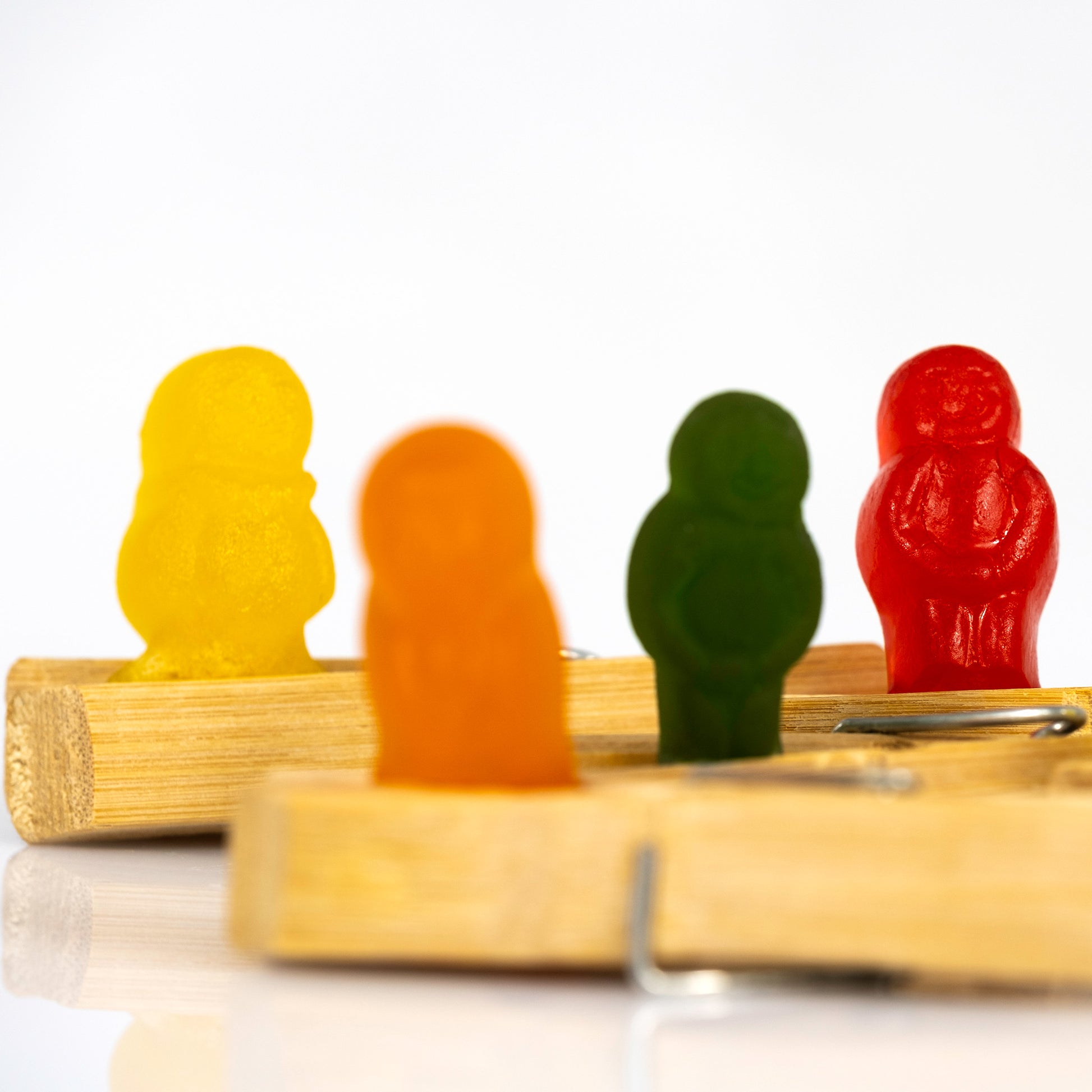 Close-up of yellow, orange, green and red gummy figures standing between wooden clothes pegs with selective shallow focus.