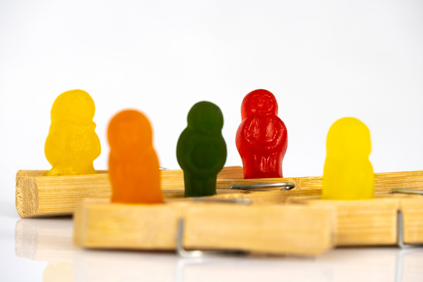 Five colourful gummy figures arranged at different depths among wooden clothes pegs against a white background.