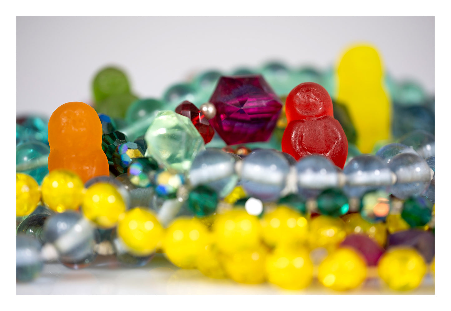 Colourful gummy figures partially hidden among layers of bright beads, jewellery and translucent faceted objects.