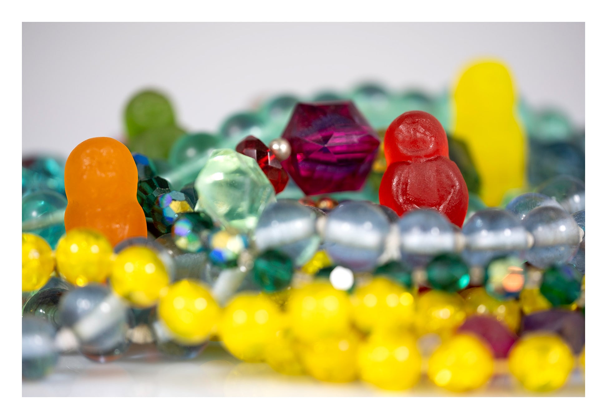 Colourful gummy figures partially hidden among layers of bright beads, jewellery and translucent faceted objects.