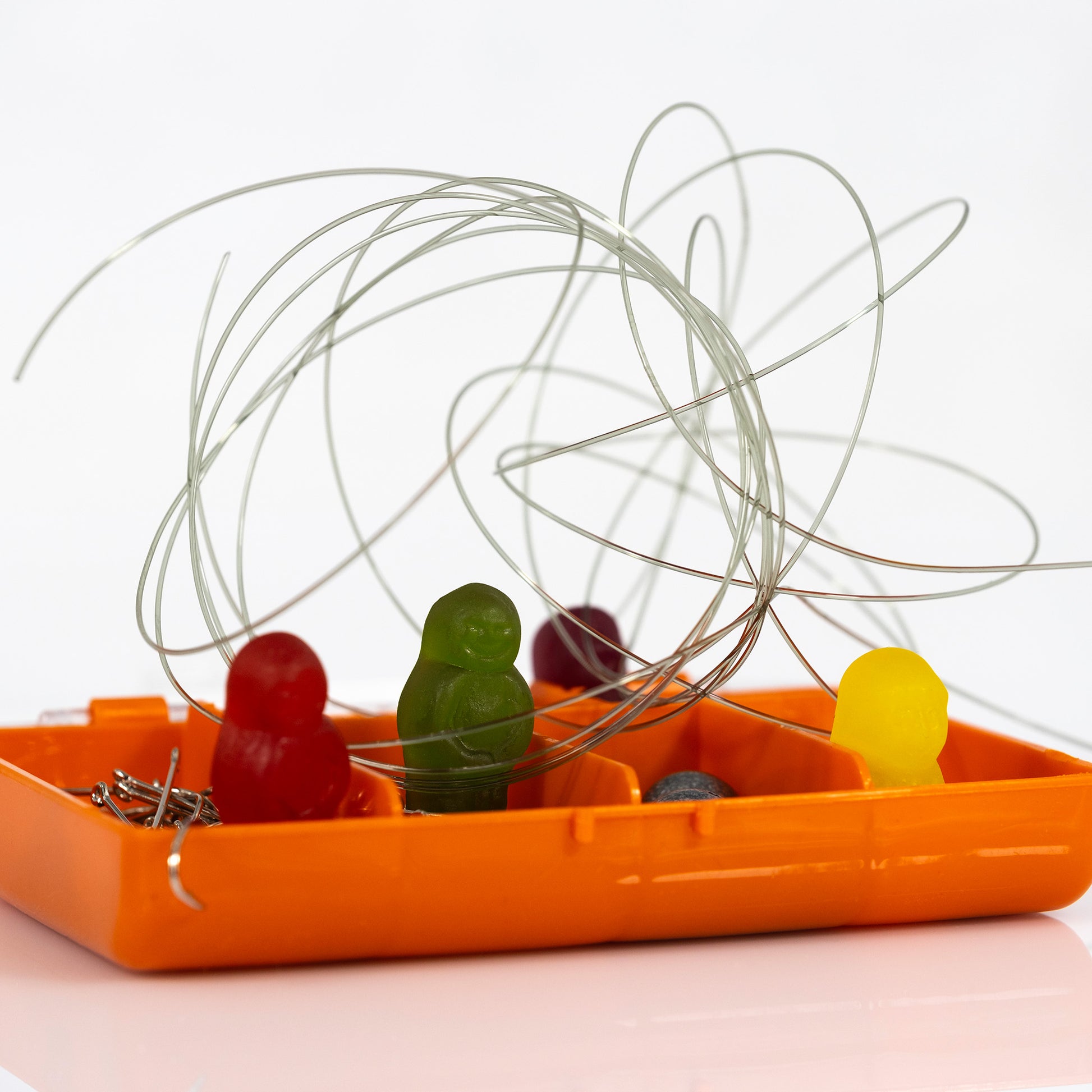 Close-up of red, green and yellow gummy figures inside an orange tackle box beneath tangled loops of fishing line.