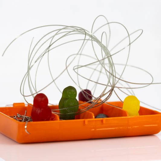 Close-up of red, green and yellow gummy figures inside an orange tackle box beneath tangled loops of fishing line.