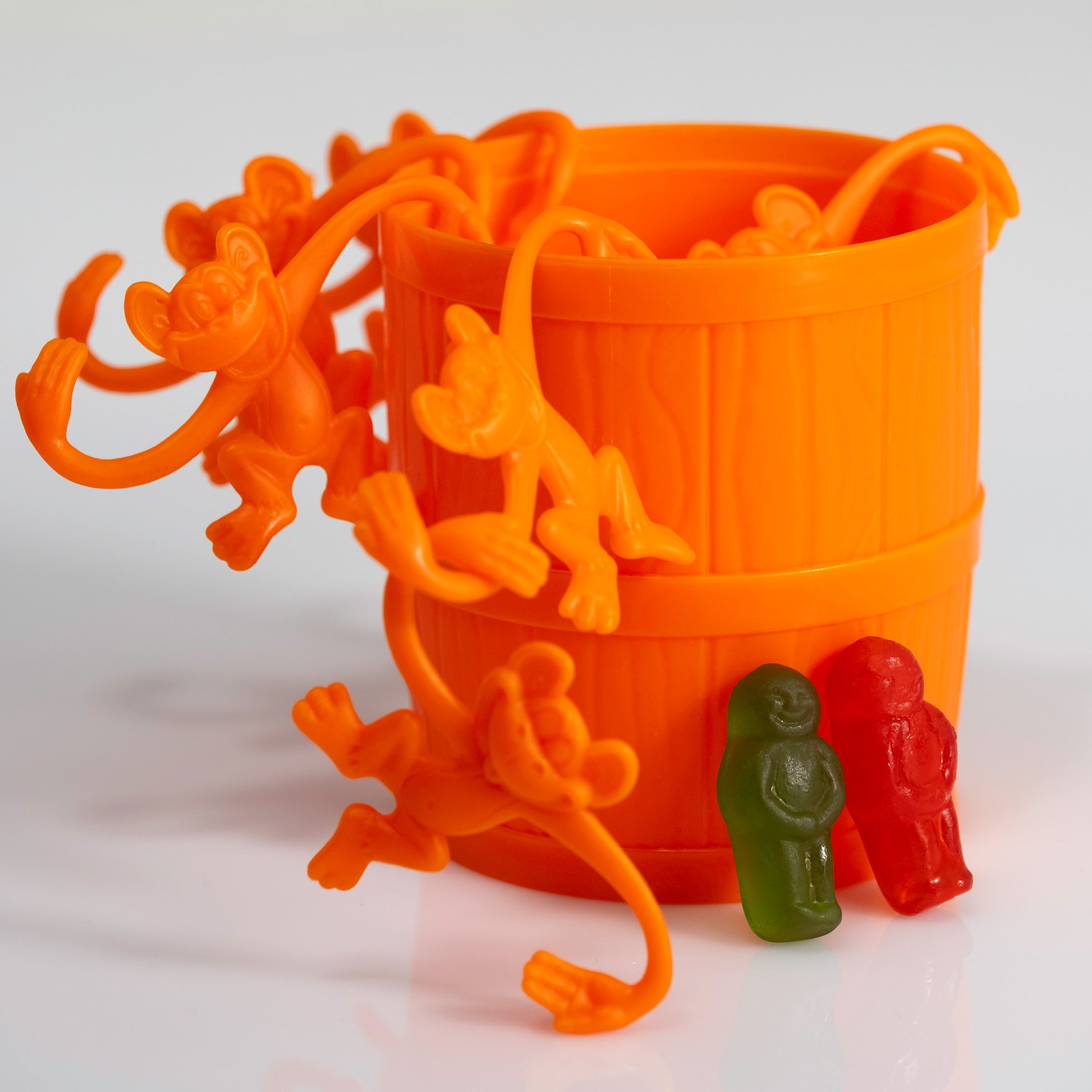 Orange monkeys climbing and hanging around a matching barrel while two contrasting gummy figures stand beside them.
