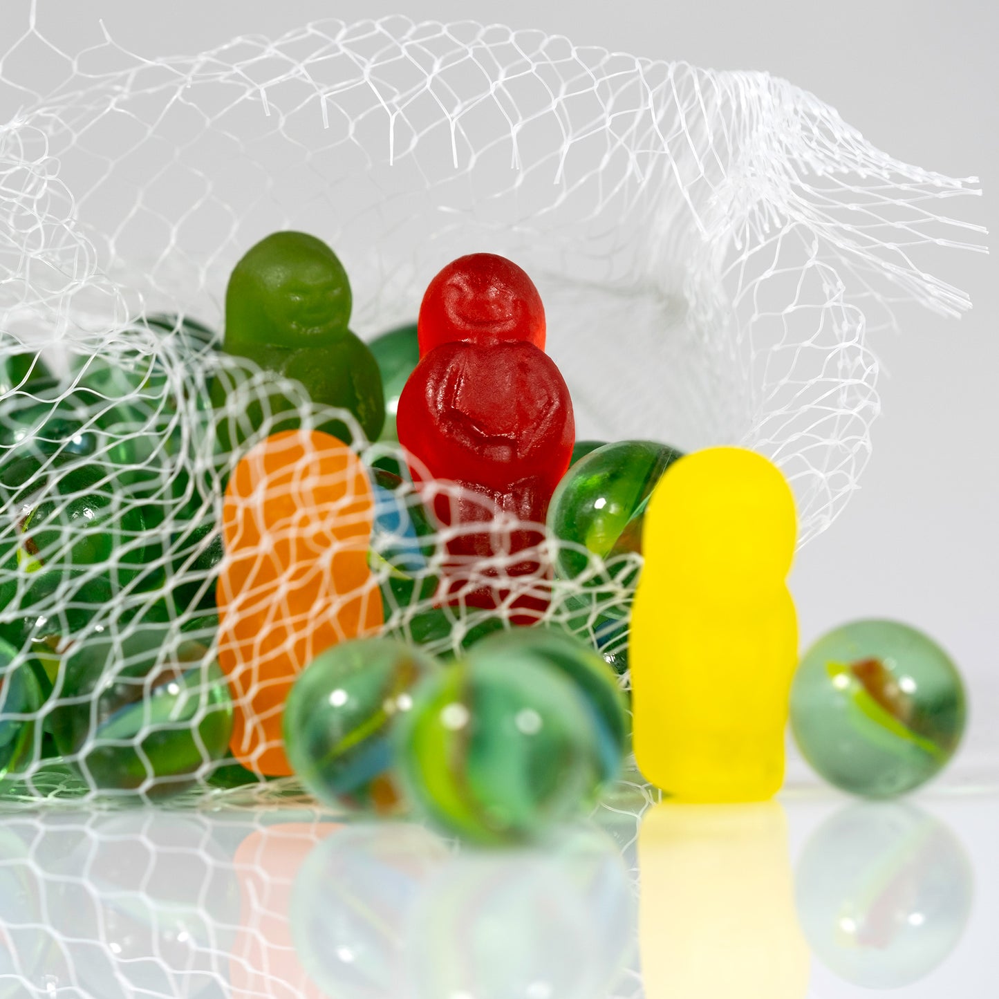 Close view of colourful gummy figures and glass marbles emerging through an open white mesh bag.