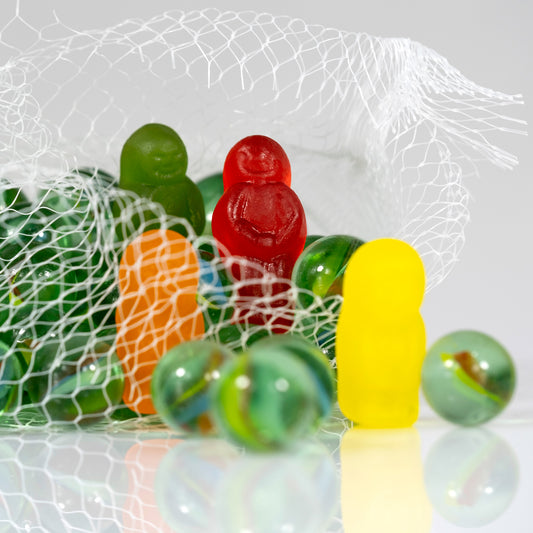 Close view of colourful gummy figures and glass marbles emerging through an open white mesh bag.