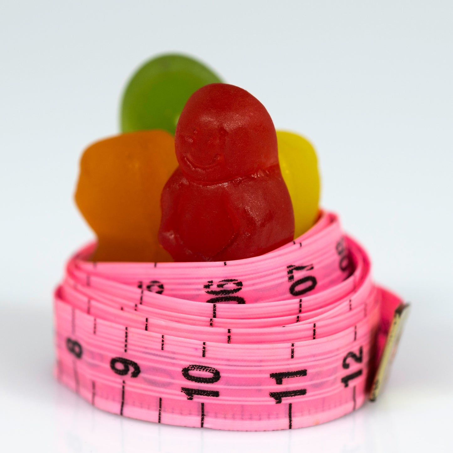 Close-up of colourful gummy figures contained within a bright pink measuring tape marked with black numbers.
