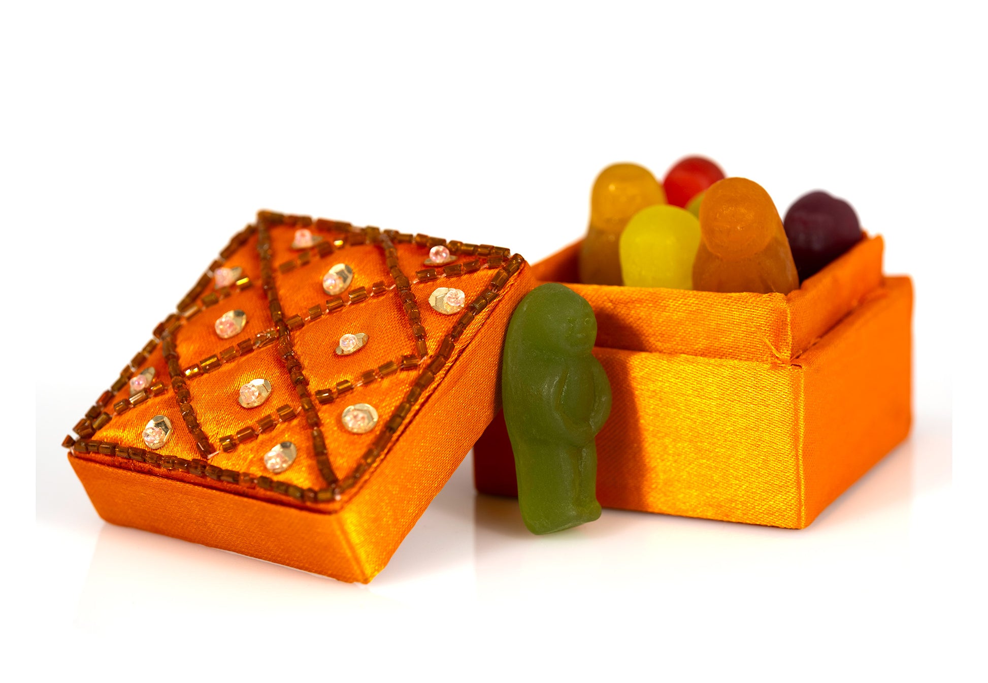 Colourful gummy figures gathered inside an open orange decorative box while a green figure stands outside beside the embellished lid.