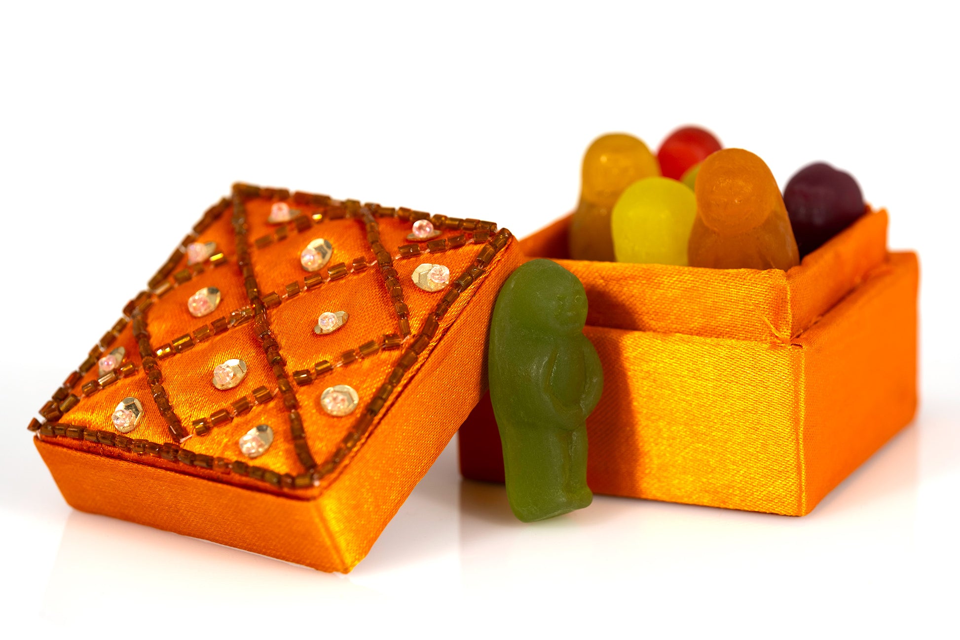 Orange decorative box with its embellished lid open, colourful gummy figures inside and a solitary green gummy figure standing outside.