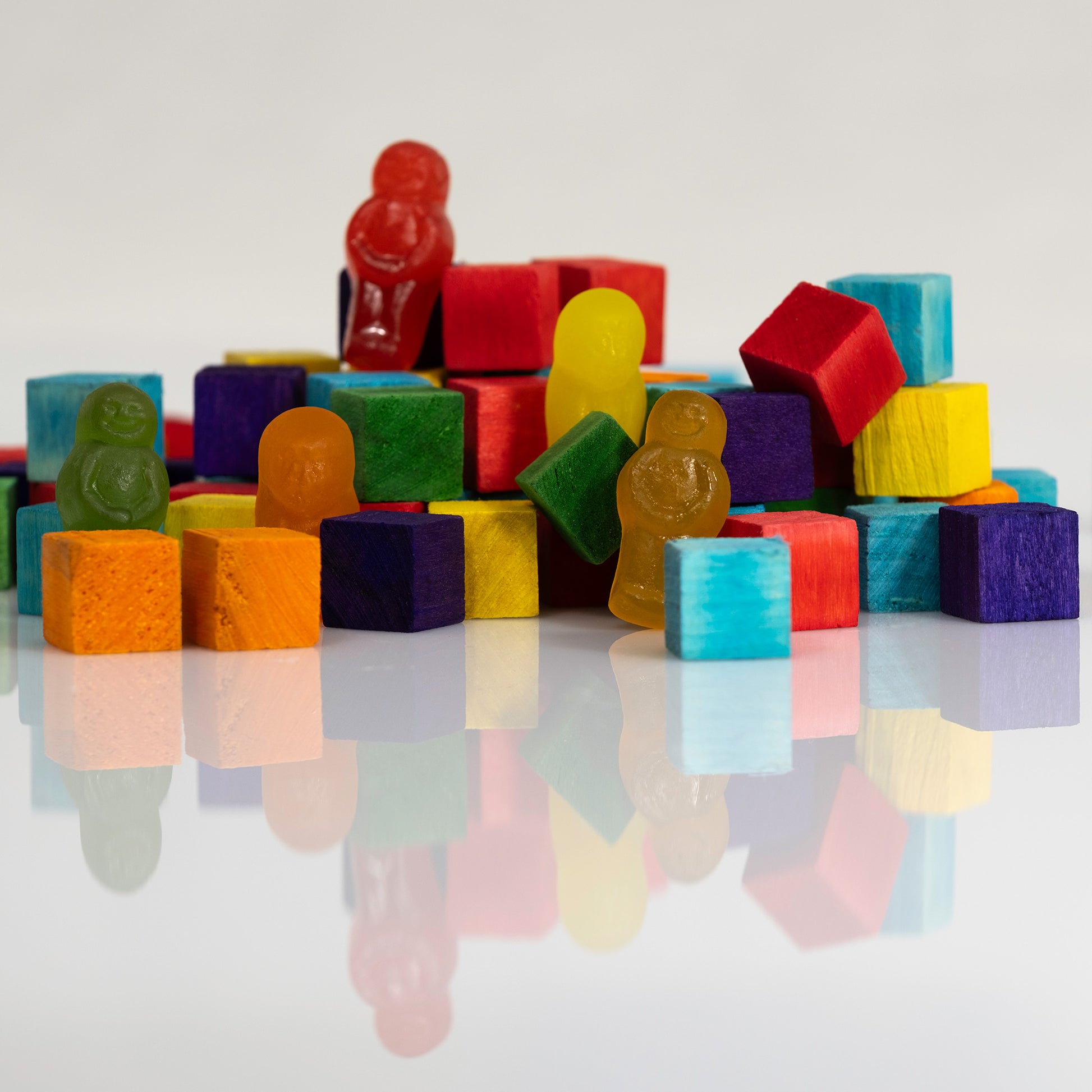 Close view of colourful wooden building blocks populated by gummy figures and reflected on a glossy white surface.