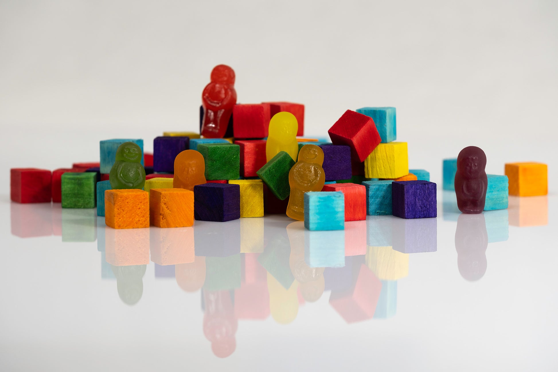 Wide still life of brightly coloured wooden blocks and gummy figures, including a solitary purple figure separated from the central group.