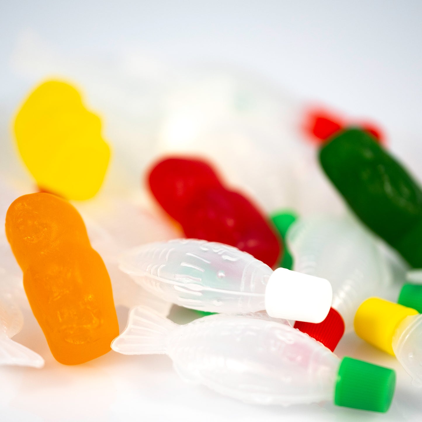Close-up of an orange gummy figure standing among translucent fish-shaped objects with colourful figures softly blurred behind.