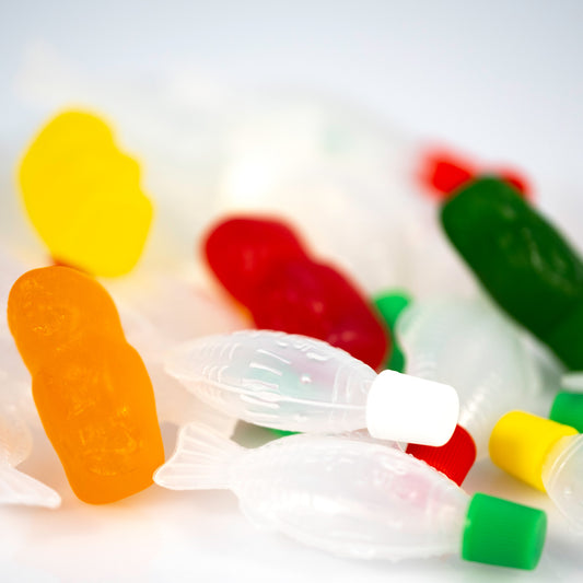 Close-up of an orange gummy figure standing among translucent fish-shaped objects with colourful figures softly blurred behind.