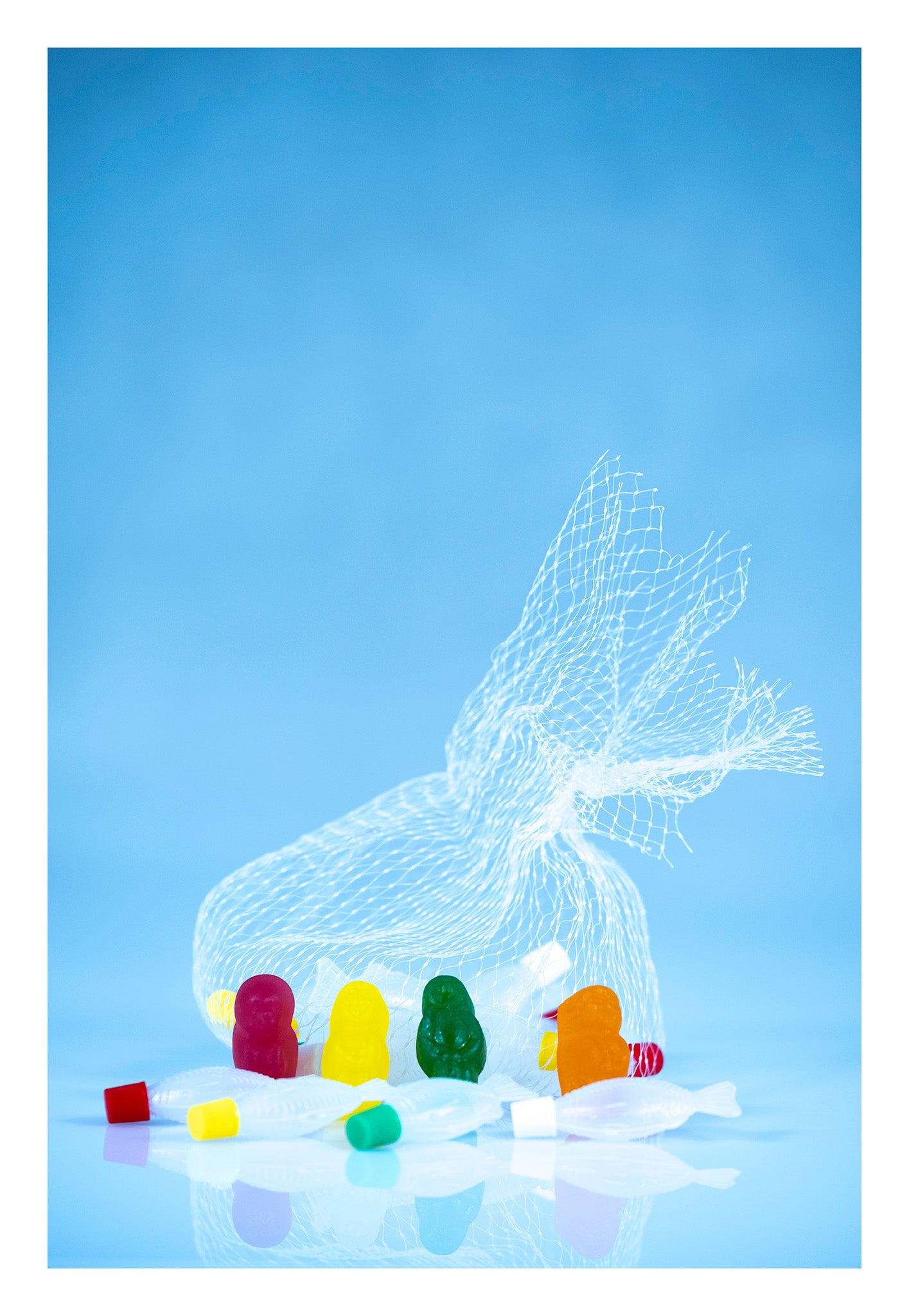 Four colourful gummy figures stand among translucent fish beneath a large white net against a bright blue background.