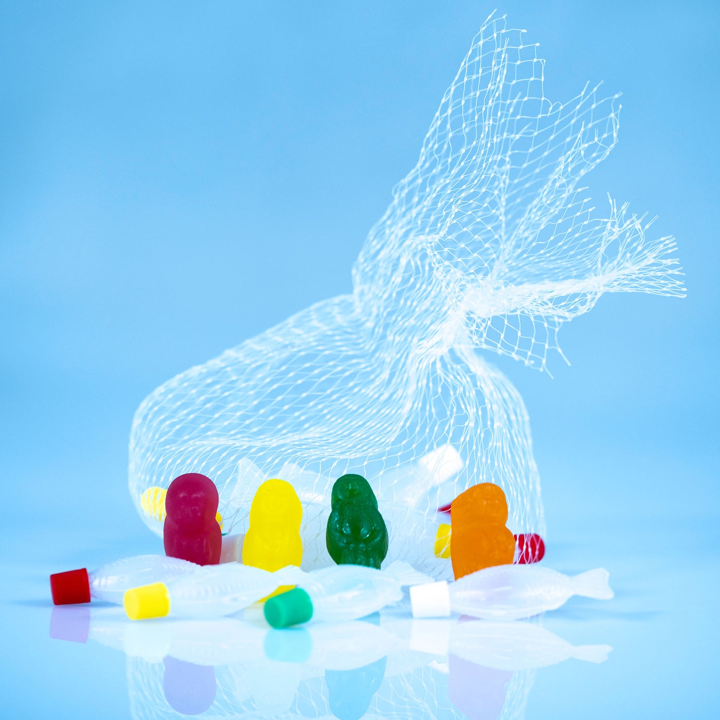 Close view of magenta, yellow, green and orange gummy figures surrounded by translucent fish beneath a large white mesh net.