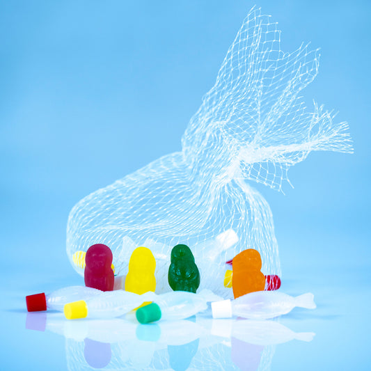 Close view of magenta, yellow, green and orange gummy figures surrounded by translucent fish beneath a large white mesh net.