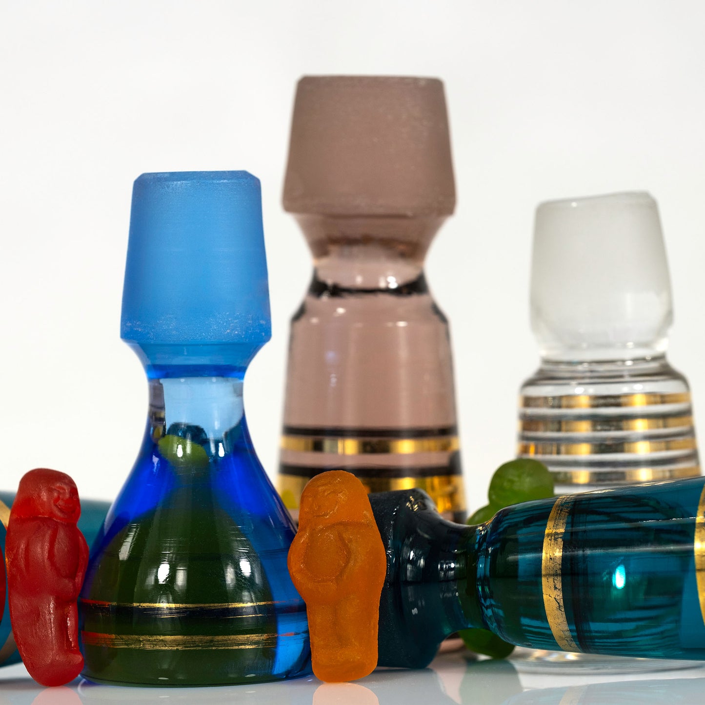 Close view of red and orange gummy figures surrounded by blue, green, pink and clear vintage glass stoppers.