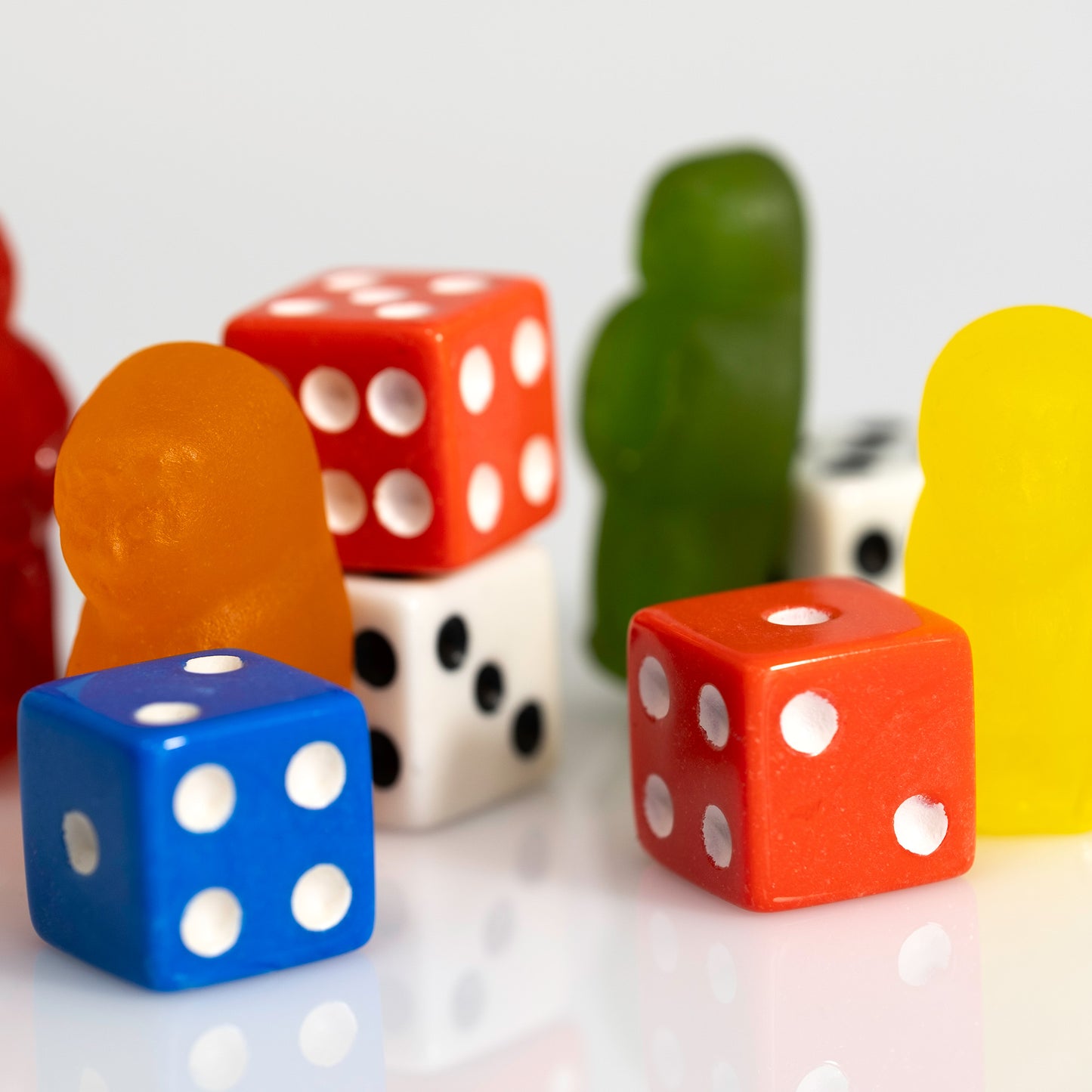 Close-up of blue and orange-red dice surrounded by orange, yellow, green and red gummy figures.