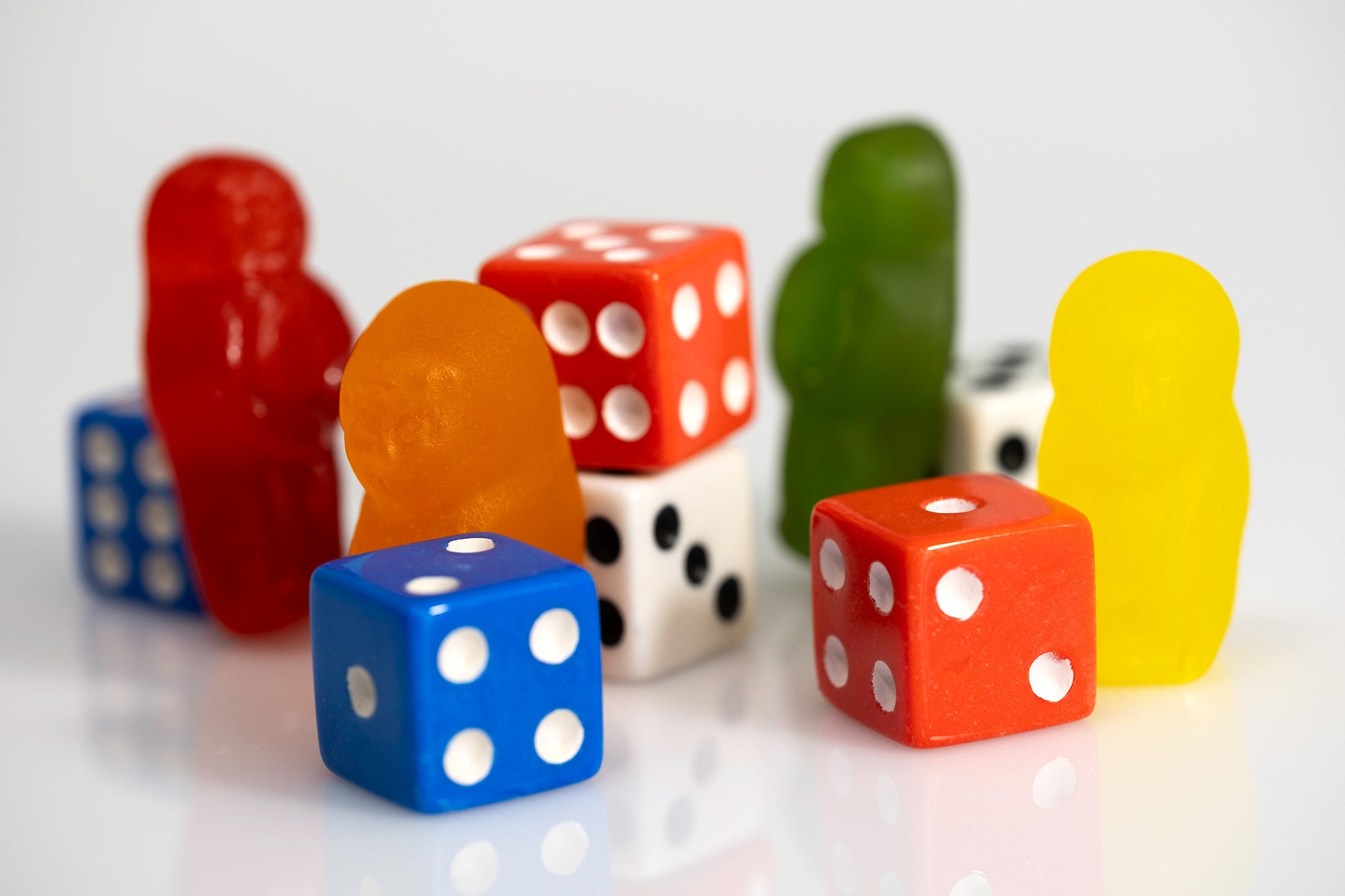 Bright gummy figures standing among colourful dice in a playful conceptual still-life photograph.
