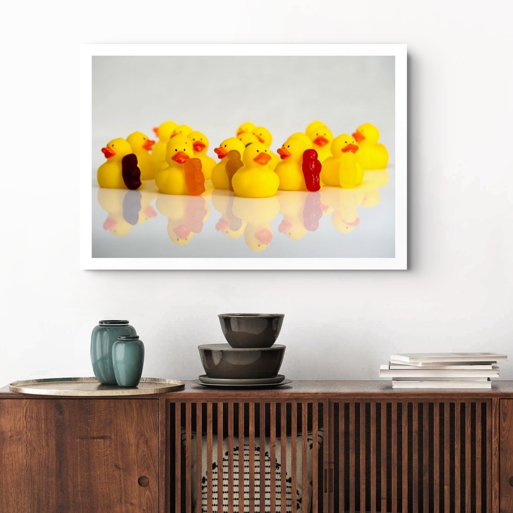 Colourful photographic artwork featuring a crowd of yellow rubber ducks and small figures displayed above a dark timber cabinet.