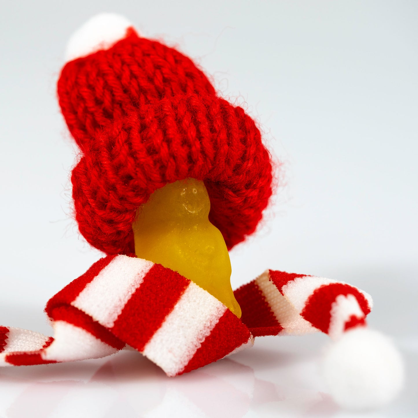 Close-up of a translucent yellow miniature figure beneath an oversized red knitted Santa hat and striped scarf.