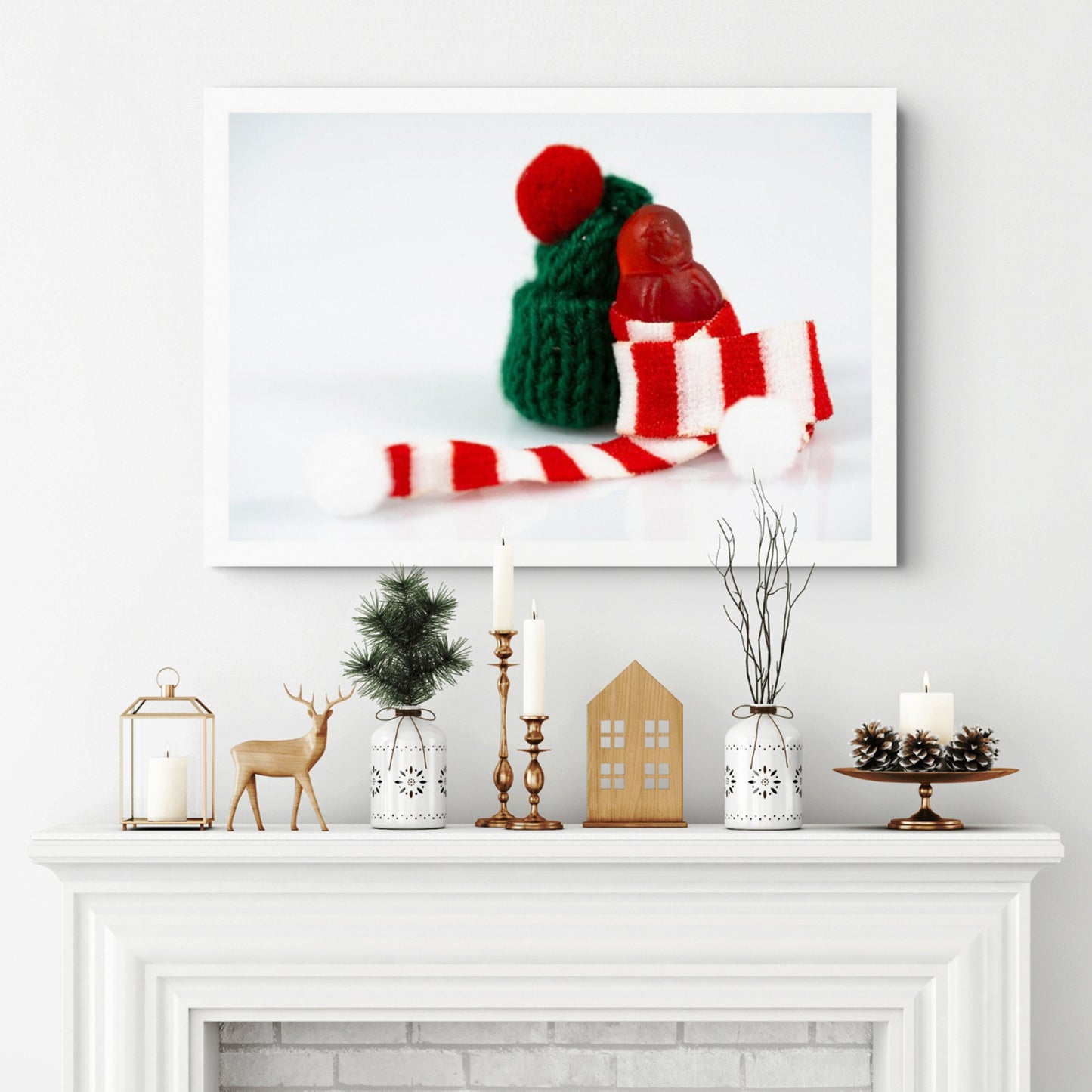 Santa Babies photographic artwork featuring a tiny red figure wrapped in a striped Christmas scarf displayed above a white fireplace.