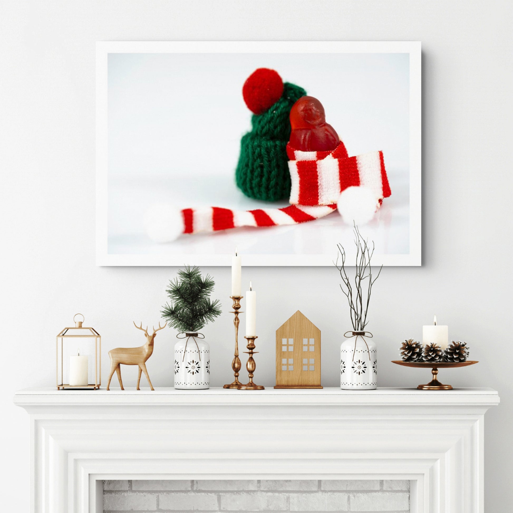 Santa Babies photographic artwork featuring a tiny red figure wrapped in a striped Christmas scarf displayed above a white fireplace.