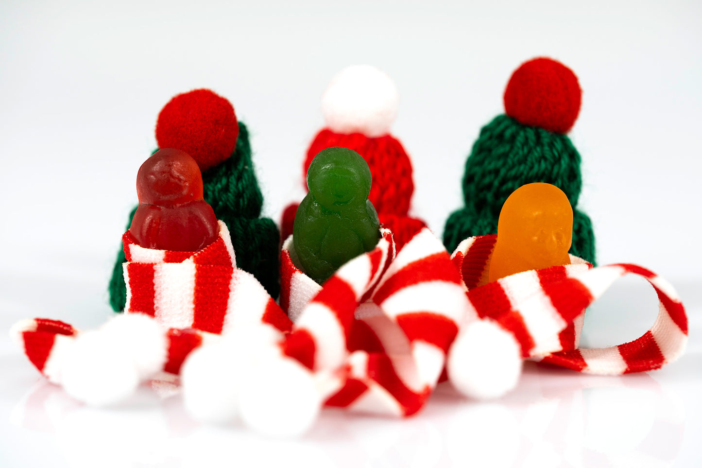 Three colourful miniature figures surrounded by striped scarves, white pompoms and red and green knitted hats.
