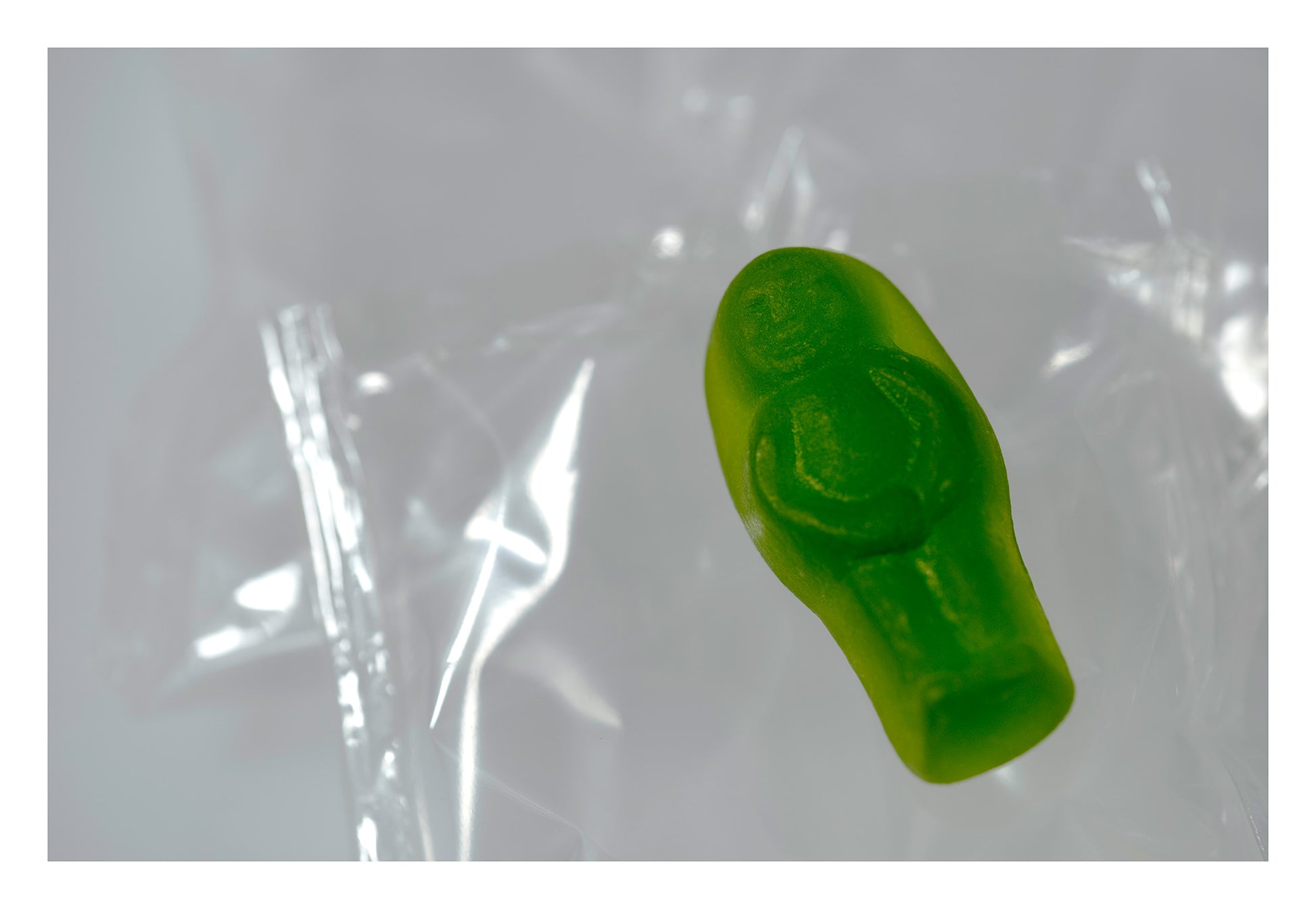 Solitary translucent green baby-shaped figure suspended against pale folded transparent material.