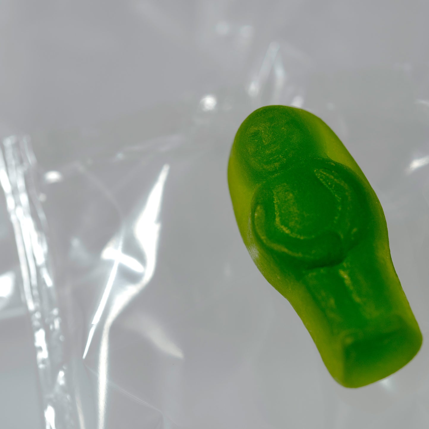 Close-up of a translucent green baby-shaped confectionery figure surrounded by reflective clear material.