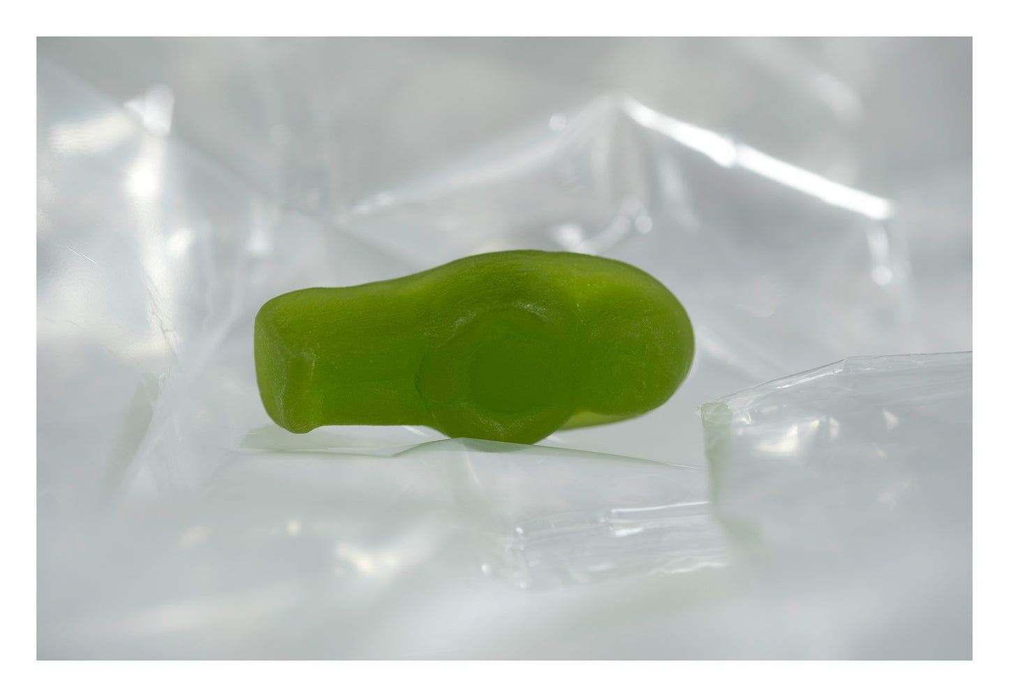 Translucent green baby-shaped figure lying on its side among pale folds of clear reflective material.