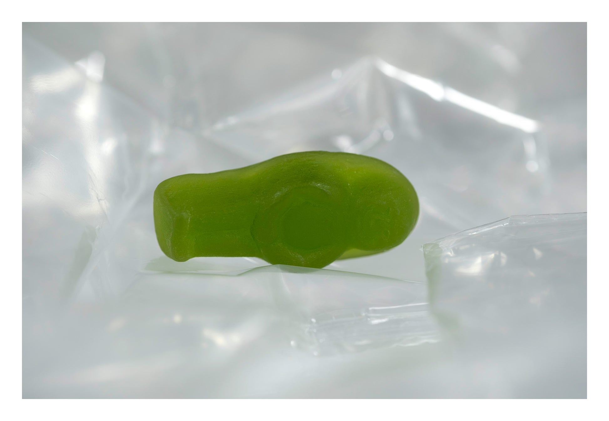Translucent green baby-shaped figure lying on its side among pale folds of clear reflective material.