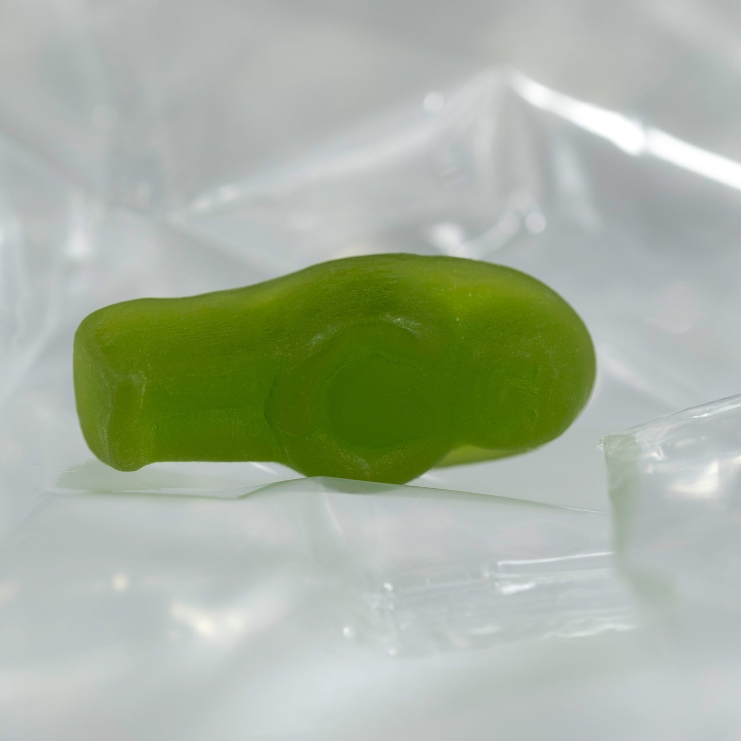 Close-up of a translucent green baby-shaped confectionery figure lying on its side against clear folded material.